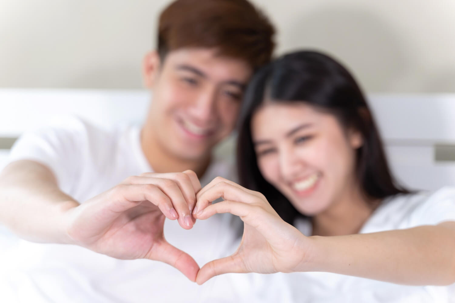 portrait-happy-young-couple-sitting-smiling-bed-hand-make-heart-shape-together